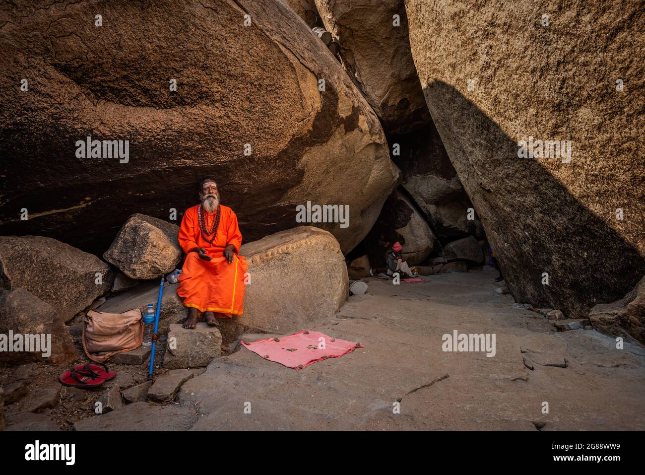 Hampi, Karnataka, India - 11 de enero de 2020 : Un monje vestido de naranja, sentado entre las piedras del Camino de Kampa Bhupa en Hampi. Foto de stock