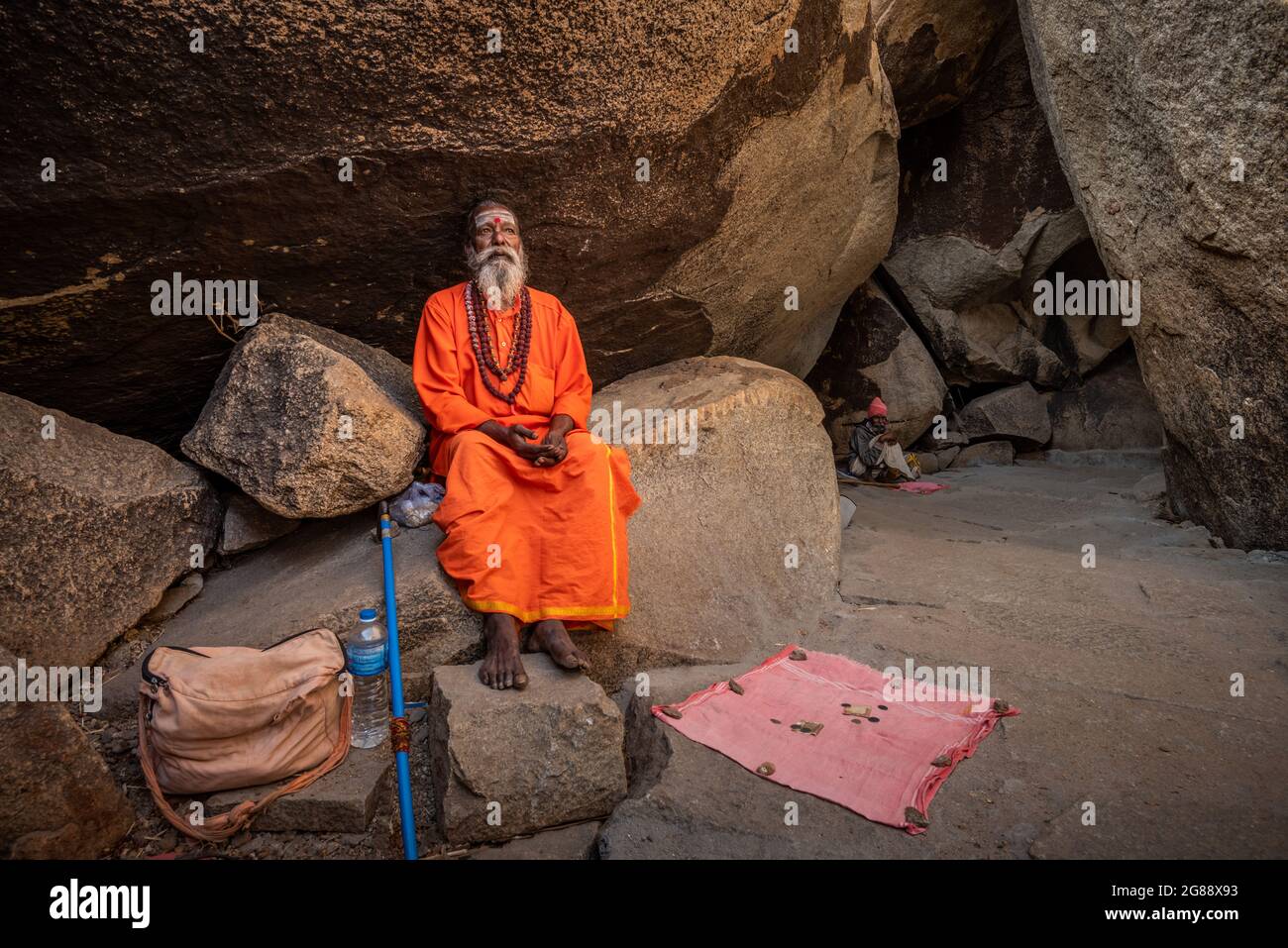 Hampi, Karnataka, India - 11 de enero de 2020 : Un monje vestido de naranja, sentado entre las piedras del Camino de Kampa Bhupa en Hampi. Foto de stock