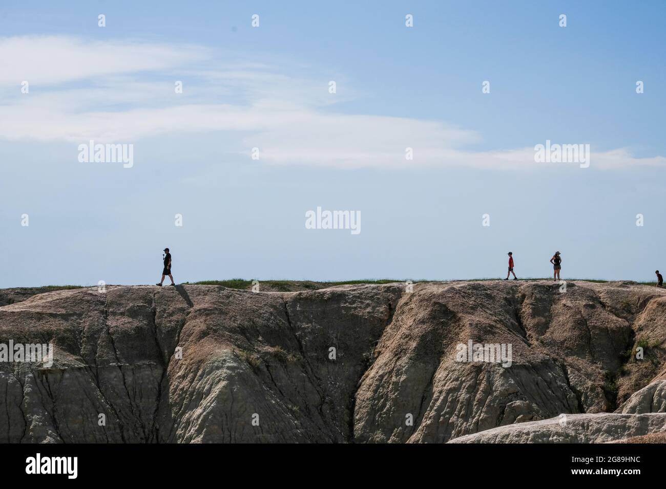 Los turistas con siluetas caminan a lo largo de una línea de cresta en el Parque Nacional Badlands, Dakota del Sur, Estados Unidos. Foto de stock