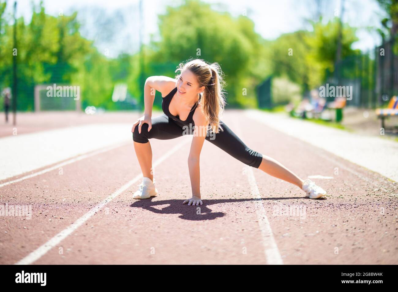 Mujer sprinter en ropa deportiva haciendo de calentamiento antes de correr en pista de estadio con revestimiento rojo aire libre Fotografía stock - Alamy