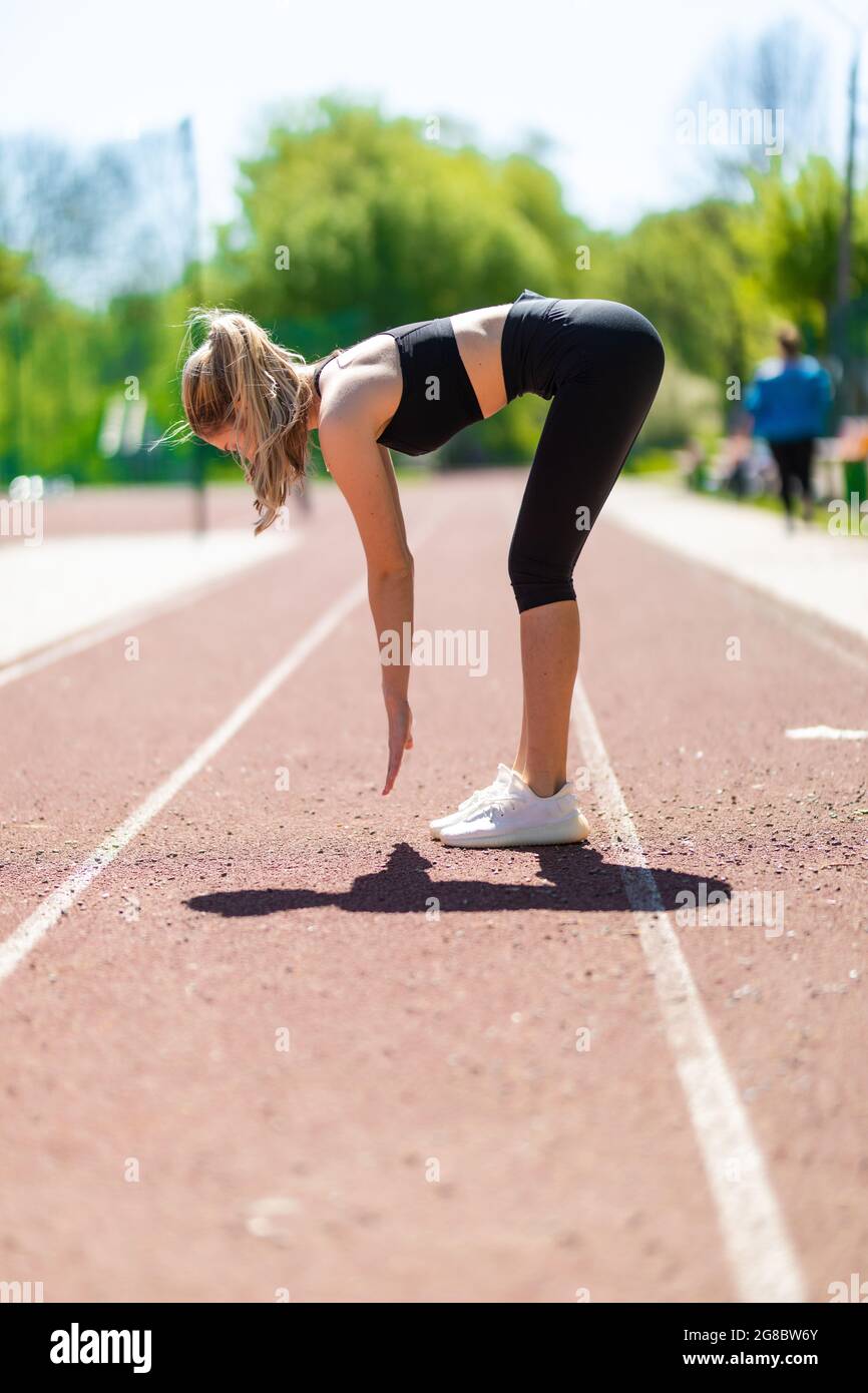 Mujer sprinter en ropa deportiva haciendo ejercicios de calentamiento antes  de correr en pista de estadio con revestimiento rojo al aire libre  Fotografía de stock - Alamy