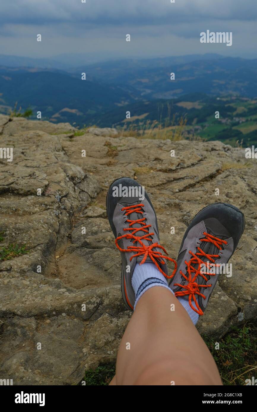 Piernas femeninas en botas de senderismo en las rocas a través de la vista aérea de las montañas y el cielo dramático. Concepto de actividades al aire libre Foto de stock