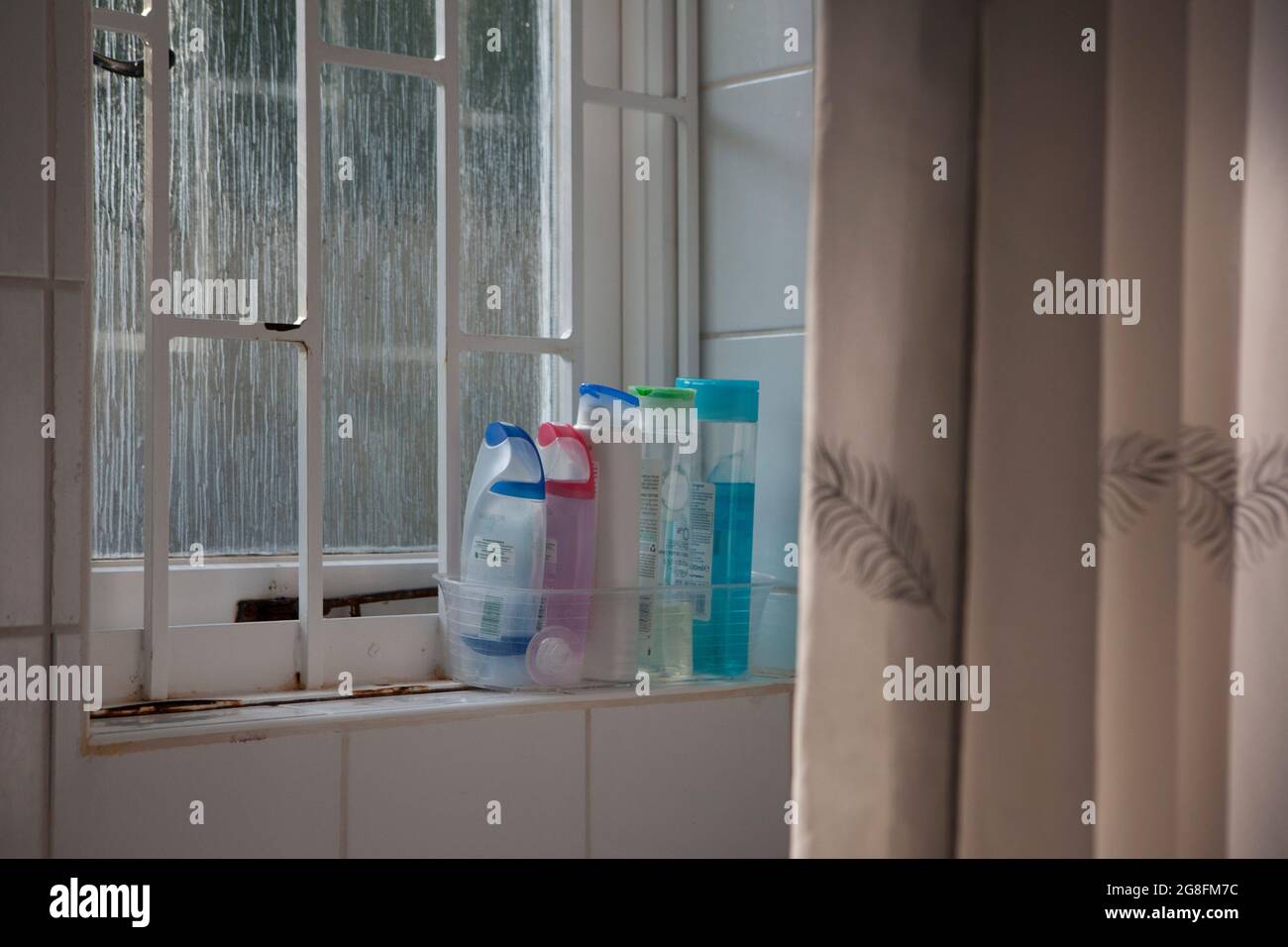 East Sussex, Reino Unido, 17 de julio de 2021: Botellas de plástico de gel de ducha en un alféizar junto a una cortina de ducha. La ventana de cristal esmerilado proporciona una luz suave Foto de stock