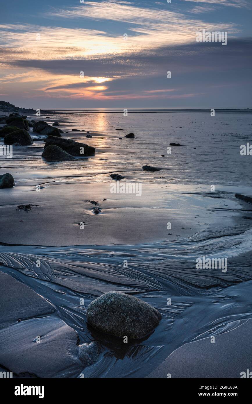 Puesta de sol sobre la costa de Solway Firth, con reflejos sobre la arena y las rocas durante una marea baja. Cerca de Allonby, al noroeste de Cumbria, Inglaterra Foto de stock