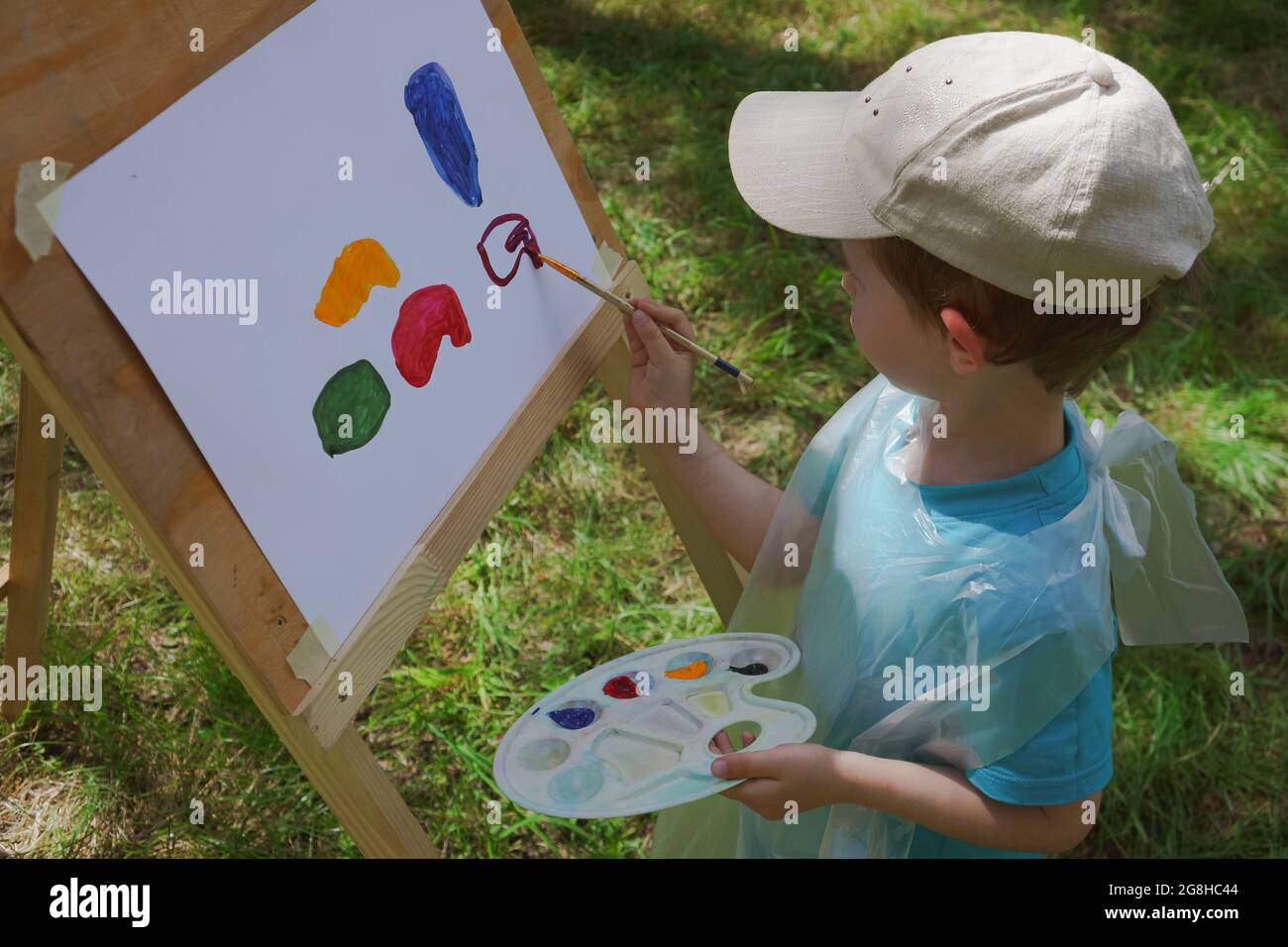 niño de 3-4 años de edad dibuja en una caballete con pinturas al aire libre Foto de stock