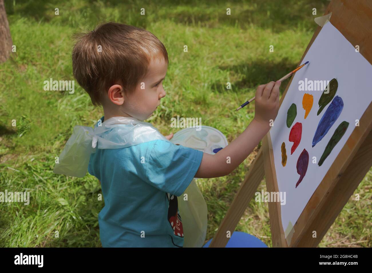 niño de 3-4 años de edad dibuja en una caballete con pinturas diligentemente al aire libre Foto de stock