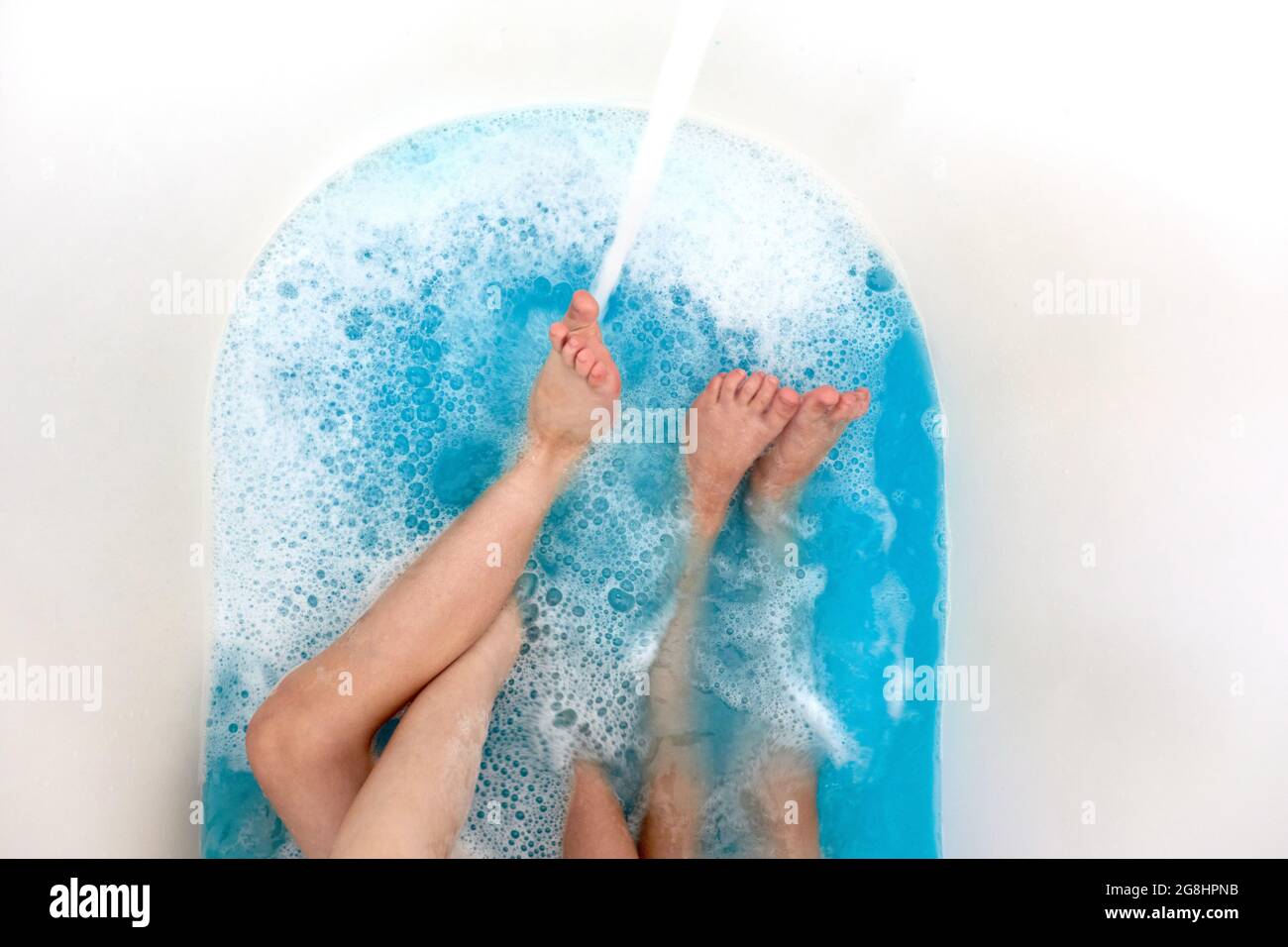Cierre las piernas de los niños en la bañera con agua azul limpia, tubo de baño con las piernas humanas en el agua Foto de stock
