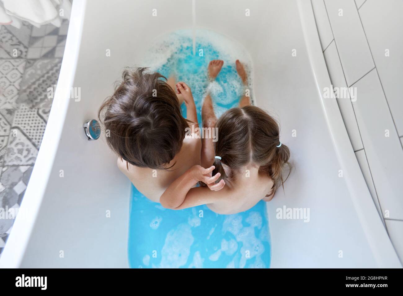 Cierre las piernas de los niños en la bañera con agua azul limpia, tubo de baño con las piernas humanas en el agua Foto de stock