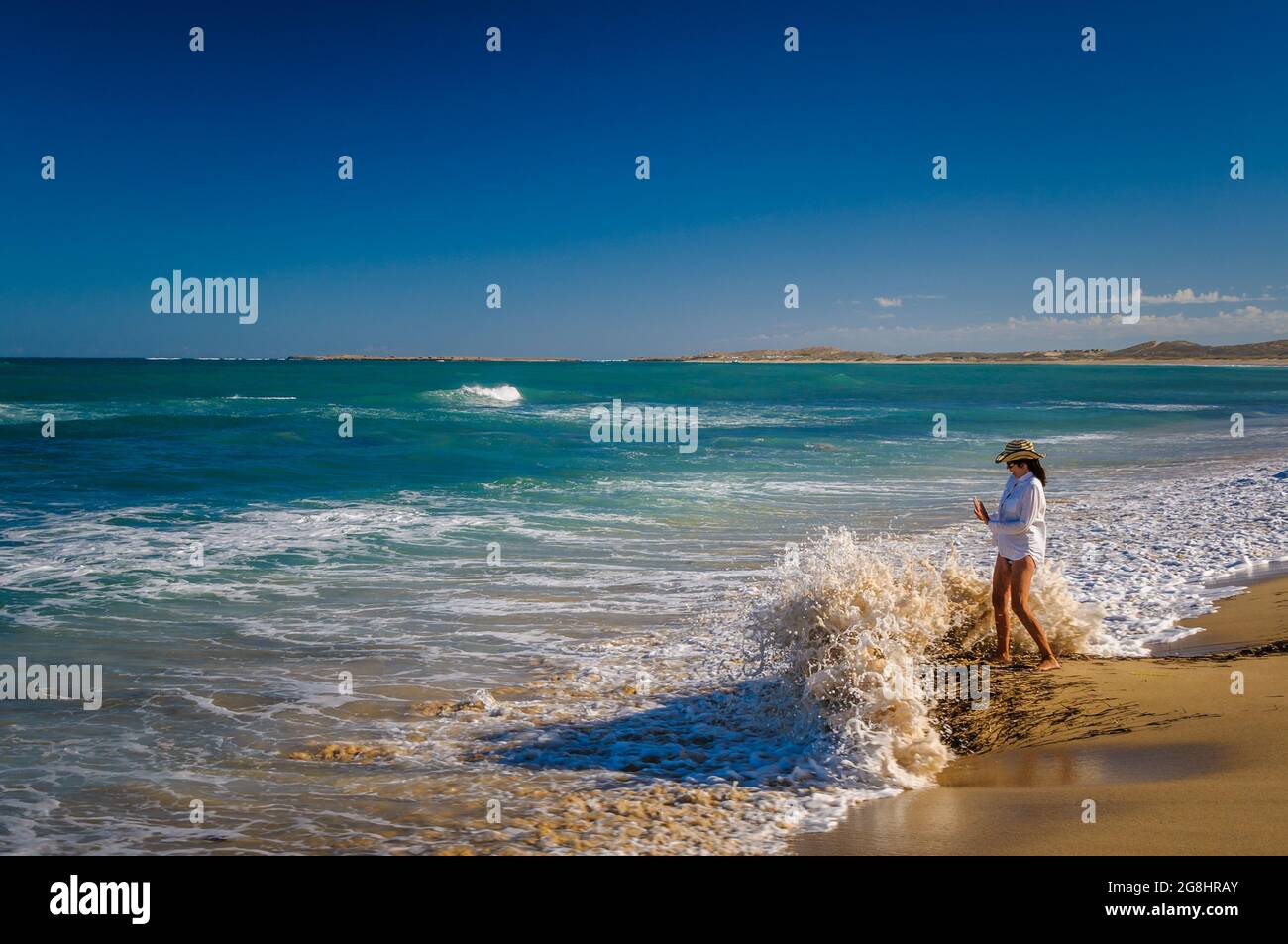 Una mujer beachcomber está en un punto arenoso sorprendido por una ola que rompe en la estación de Quobba en la región de Gascoyne de Australia Occidental. Foto de stock
