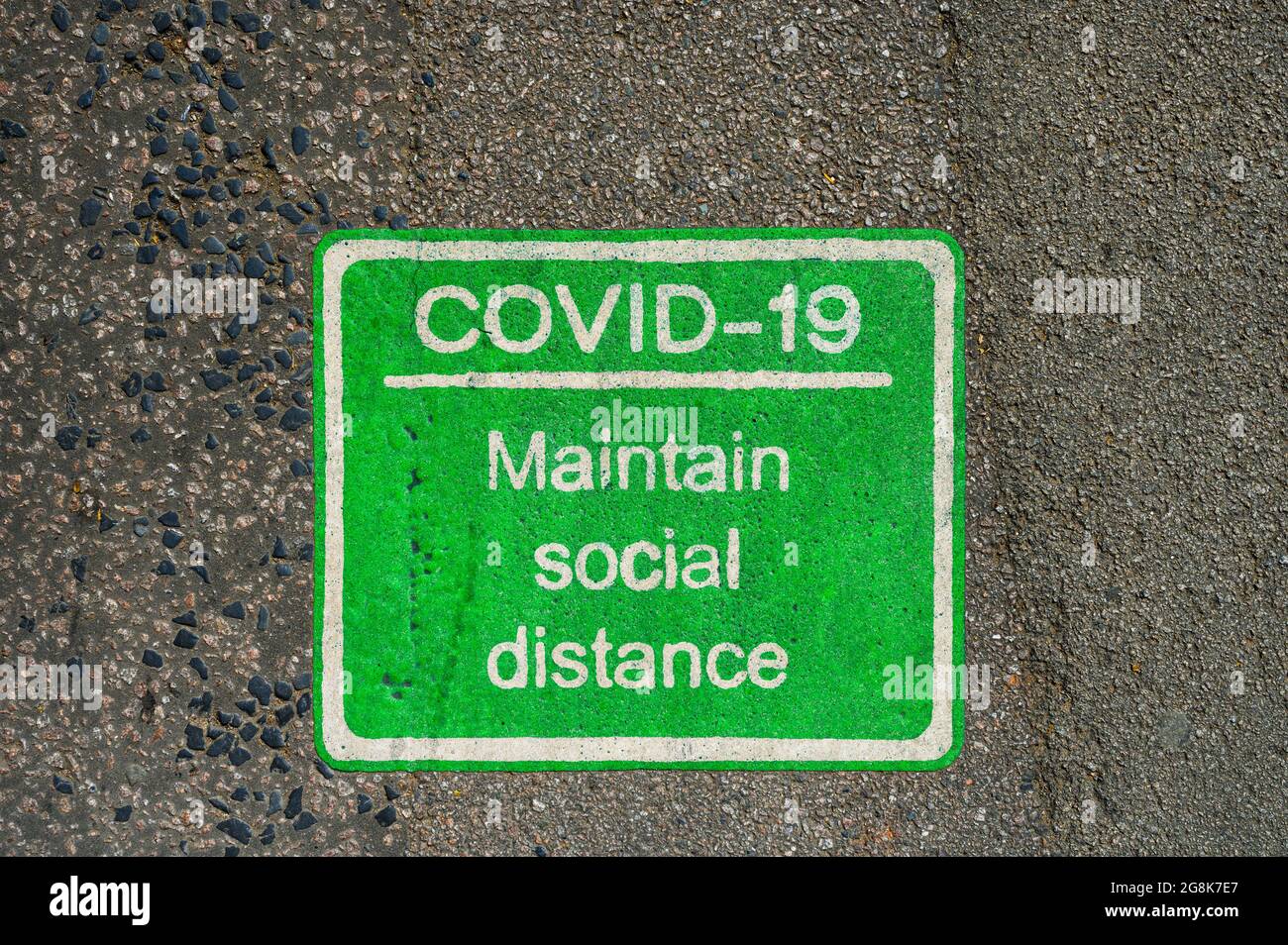 Verde COVID-19 signo de distanciamiento social pintado en pavimento o carretera. Foto de stock