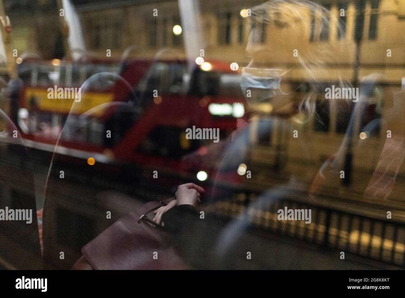 Rubia niña con máscara reflejada en la ventana del autobús por la noche, Londres, 21 de febrero de 2021 Foto de stock