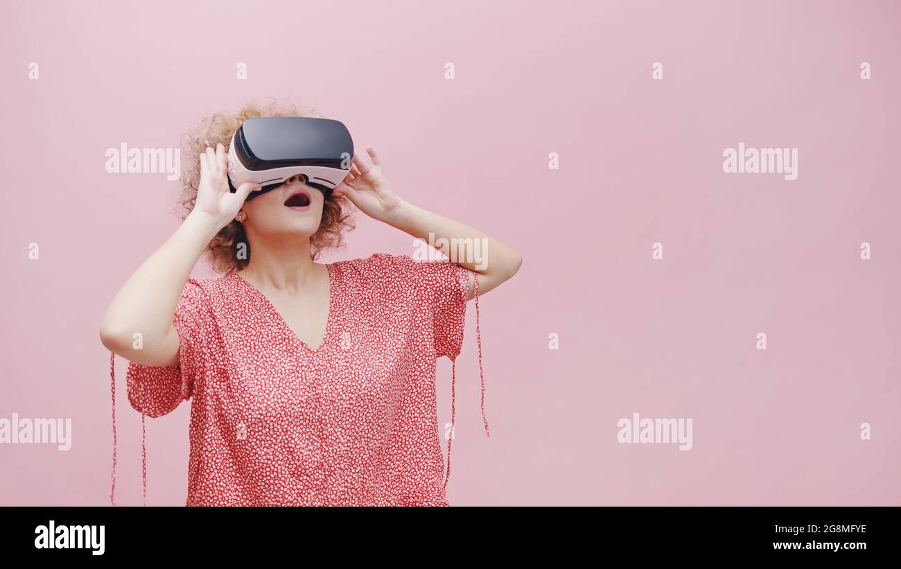 Chica usando gafas de realidad virtual VR Box viendo una película de 3D. Sentirse sorprendido. La chica se pierde en realidad virtual. Estudio sobre fondo rosa. Concepto de tecnología Fotografía de