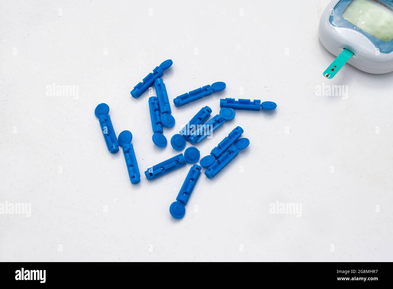 Un conjunto de lancetas azules o agujas para la monitorización del azúcar  en la sangre de la glucosa diabética. Un glucómetro se puede ver  parcialmente con una tira enchufada para una lectura