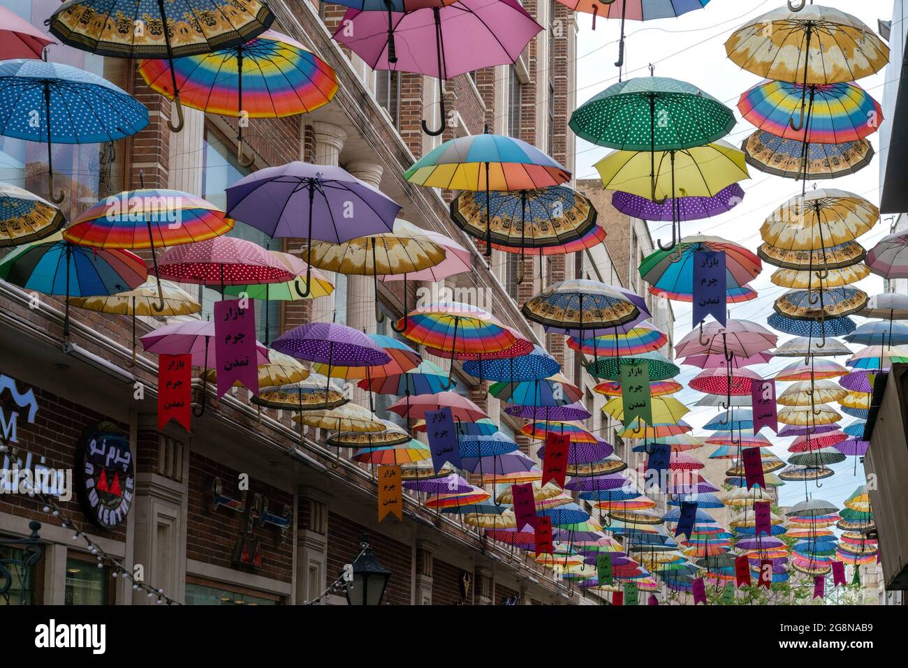 Teherán, Irán - 04.25.2019: Un montón de paraguas coloridos colgando abierto por encima de la calle lateral de Teherán, Irán. Arte callejero persa Foto de stock