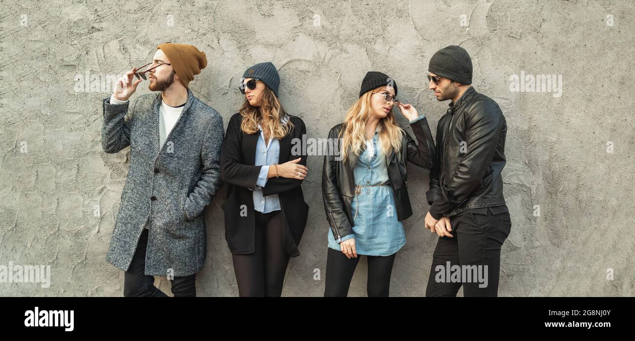 Jóvenes urbanos con gafas de sol, ropa de abrigo y gorro de lana posando contra una pared de hormigón en la calle Foto de stock