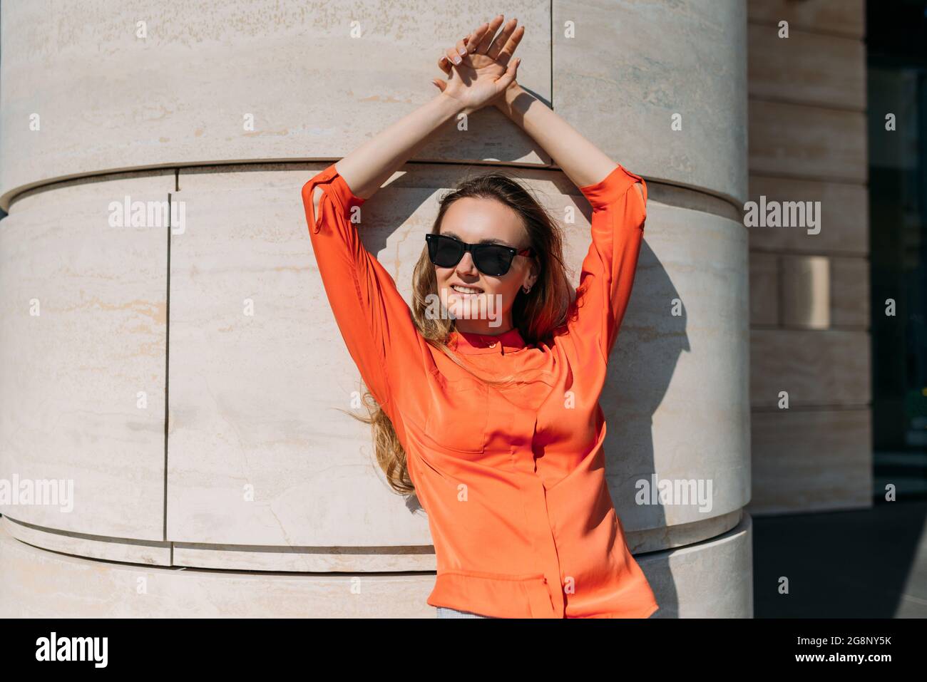 Chica caucásica con gafas de sol y ropa informal apoyada en el edificio Foto de stock
