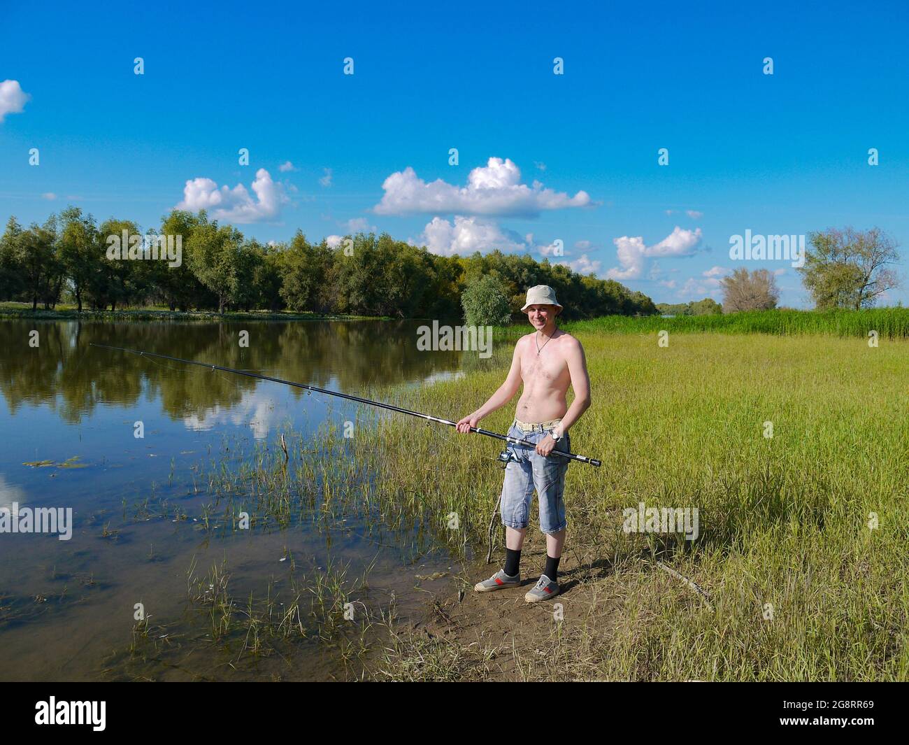 Un hombre con caña de pescar está pescando en un río de pueblo. El concepto de seguir un estilo de vida saludable en la naturaleza. Foto de stock