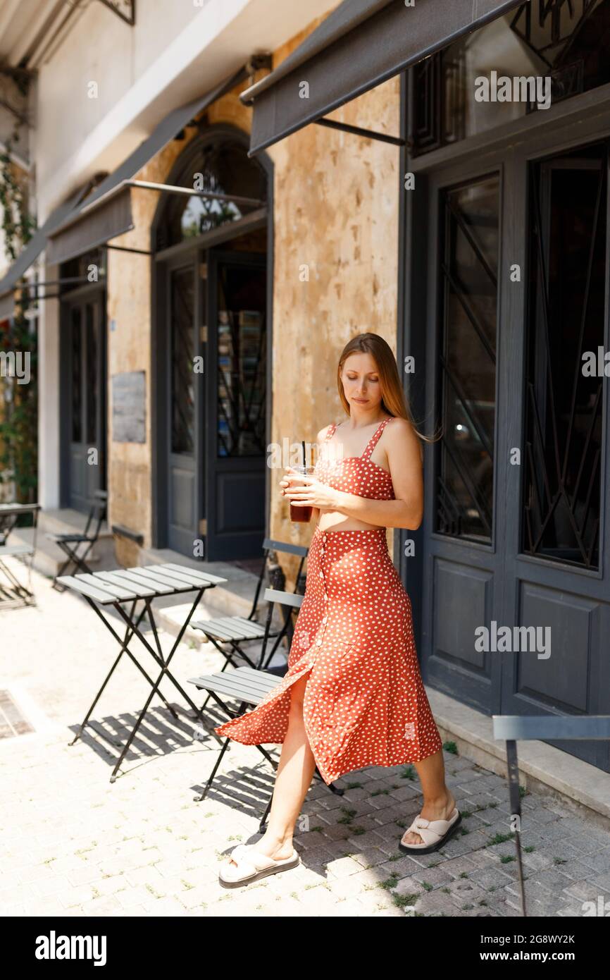 Alegre mujer joven hipster en la falda salir de la elegante cafetería, la  vieja ciudad de beber en la calle, la celebración de una taza de café por  la mañana a la
