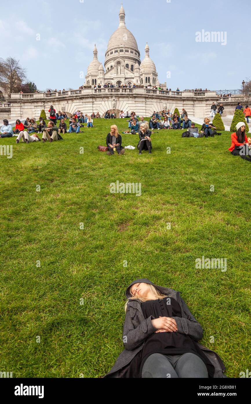Mujer joven durmiendo en un césped al pie de la Basílica del Sagrado Corazón de Montmartre en París Foto de stock