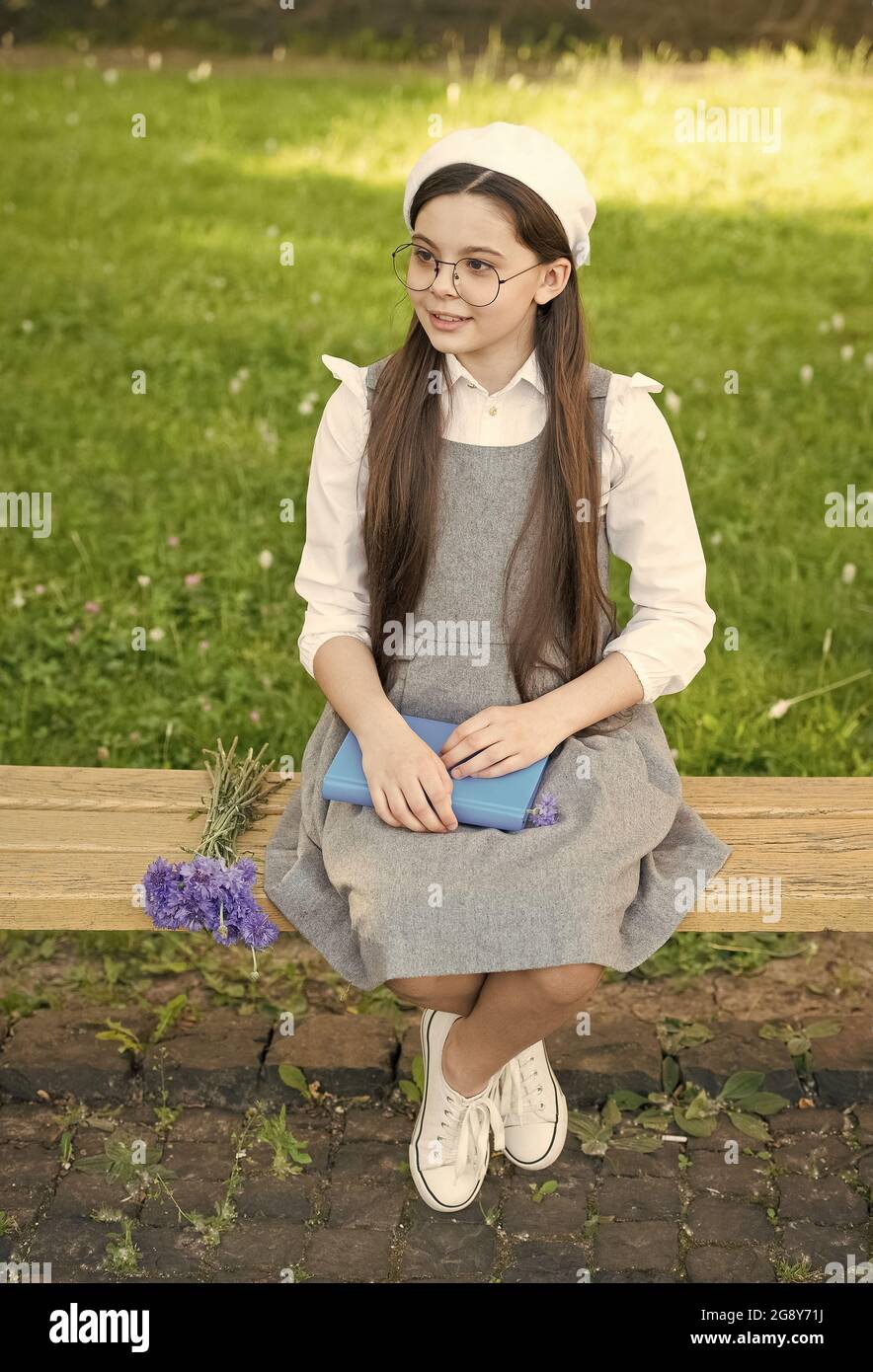 Defina su estilo. Un niño pequeño se sienta en un banco al aire libre. La  niña lleva vestido de escuela. Estilo uniforme escolar. De vuelta al estilo  de la escuela. Moda y
