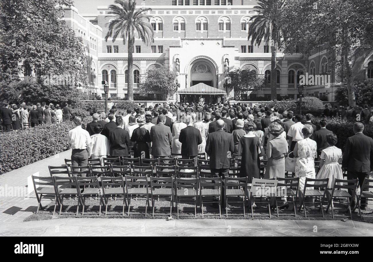 1964, histórico, en la Universidad del Sur de California (USC) se celebra una ceremonia de graduación, California, EE.UU., con los padres e invitados de pie en el área reservada para los miembros de la familia de los graduados de honor. Foto de stock