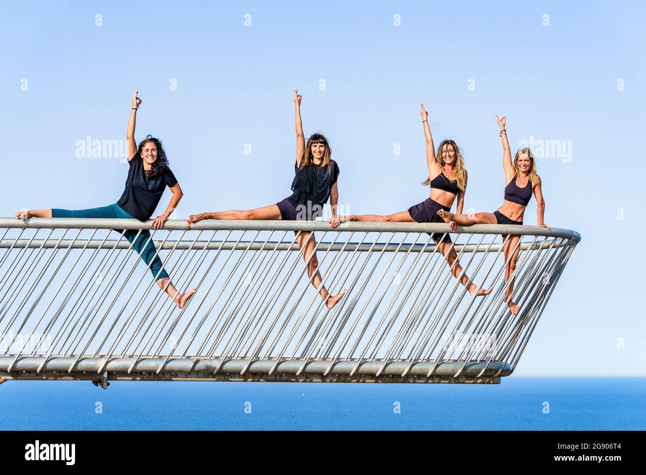 Amigas practicando actividad acrobática en la barandilla en el punto de observación sobre el mar Foto de stock