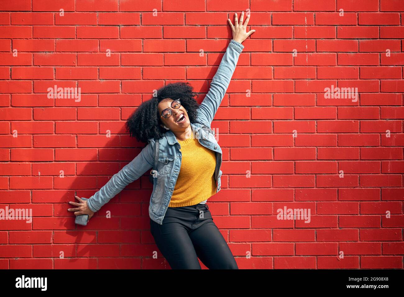 Feliz mujer joven apoyada en la pared de ladrillo rojo Foto de stock