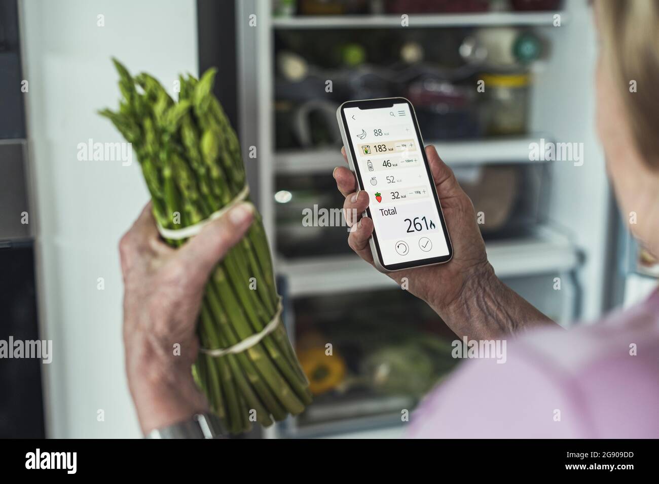Mujer calculando las calorías de los alimentos a través del teléfono inteligente en casa Foto de stock
