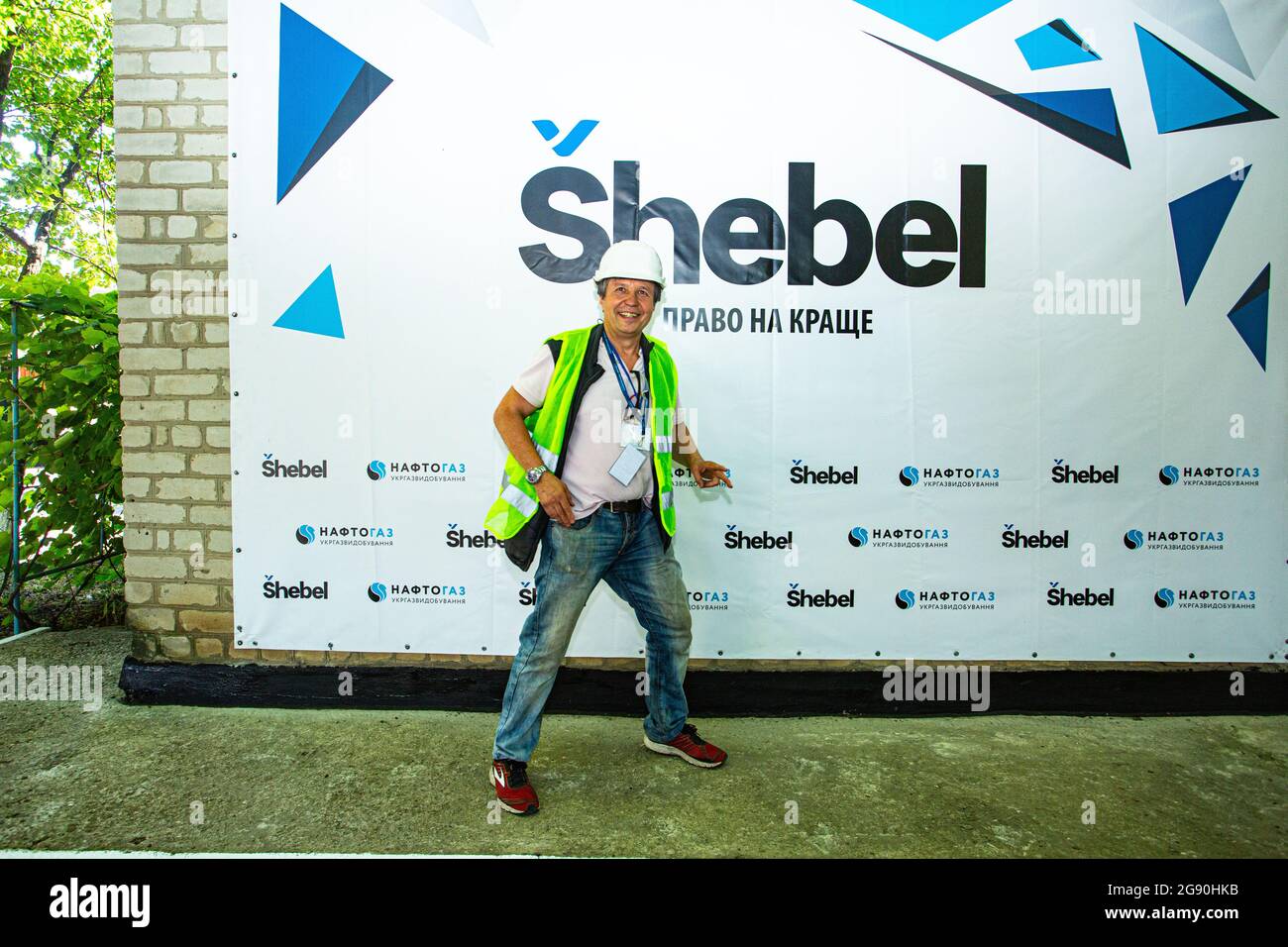 El reportero y fotógrafo ucraniano posan para la cámara contra la pared con la marca local de gasolina durante un viaje a la refinería de gas Shebelinka. Foto de stock