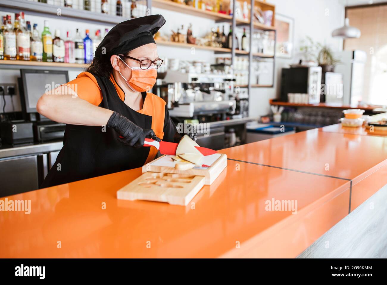 Chef mujer cortando queso manchego en el mostrador durante la pandemia Foto de stock