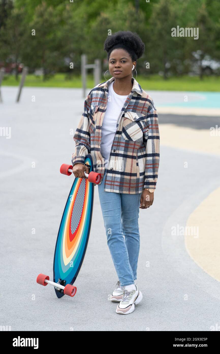 Joven africana sostiene el longboard en el parque de skate. Mujer urbana con ropa informal en skatpark stock - Alamy