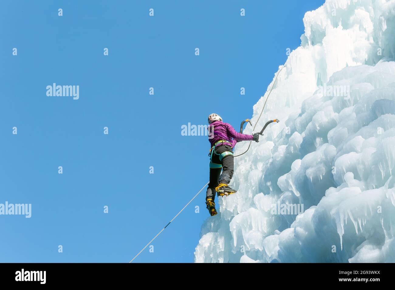 Escalador de hielo hembra en posición de tracción, haciendo pivotar los ejes de hielo sobre la cabeza y plantando la pick en el hielo, vista lateral Foto de stock