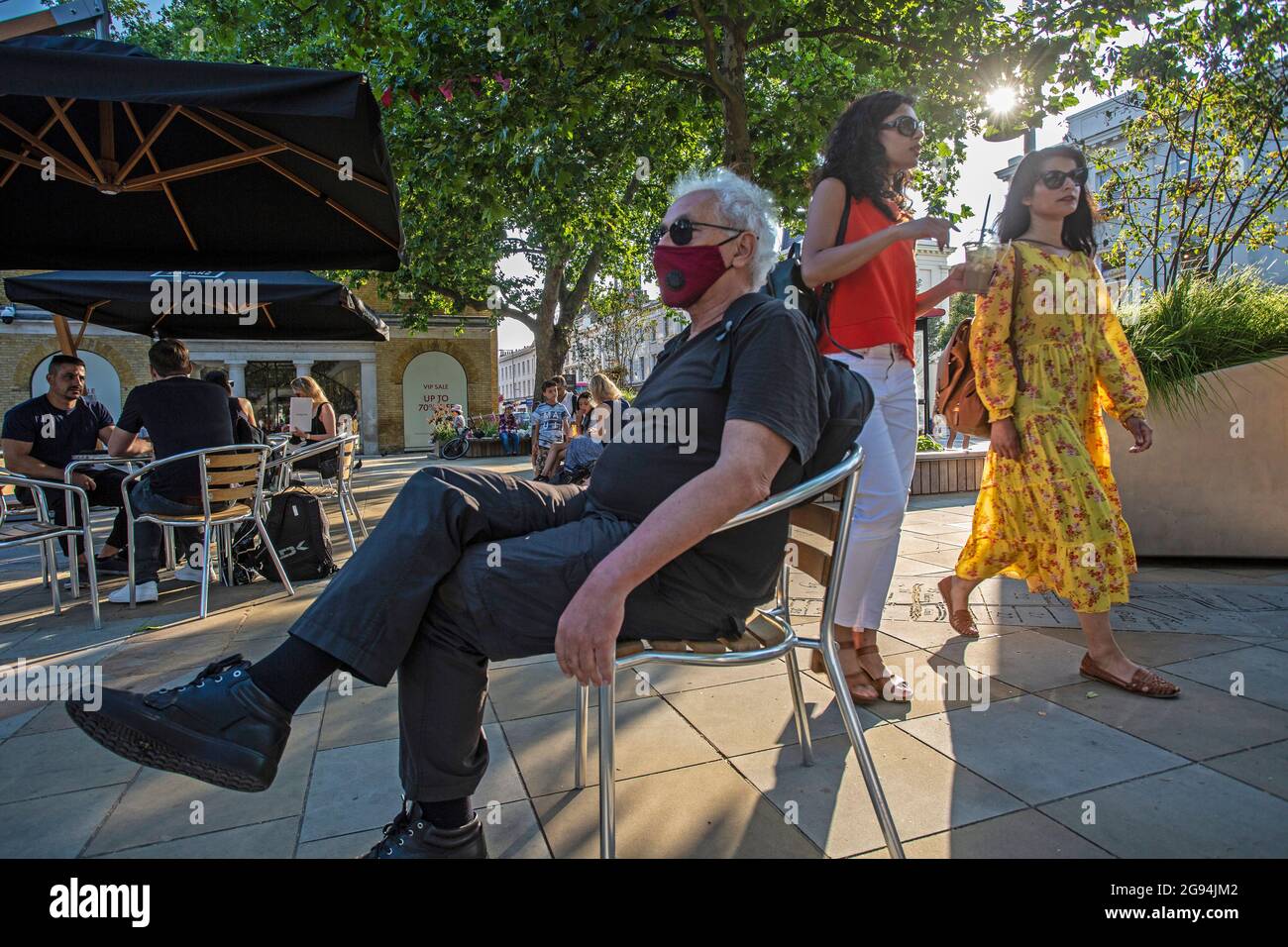 Hombre que lleva una máscara distanciando de la gente sentada cerca de King's Rd, Londres, Reino Unido Foto de stock