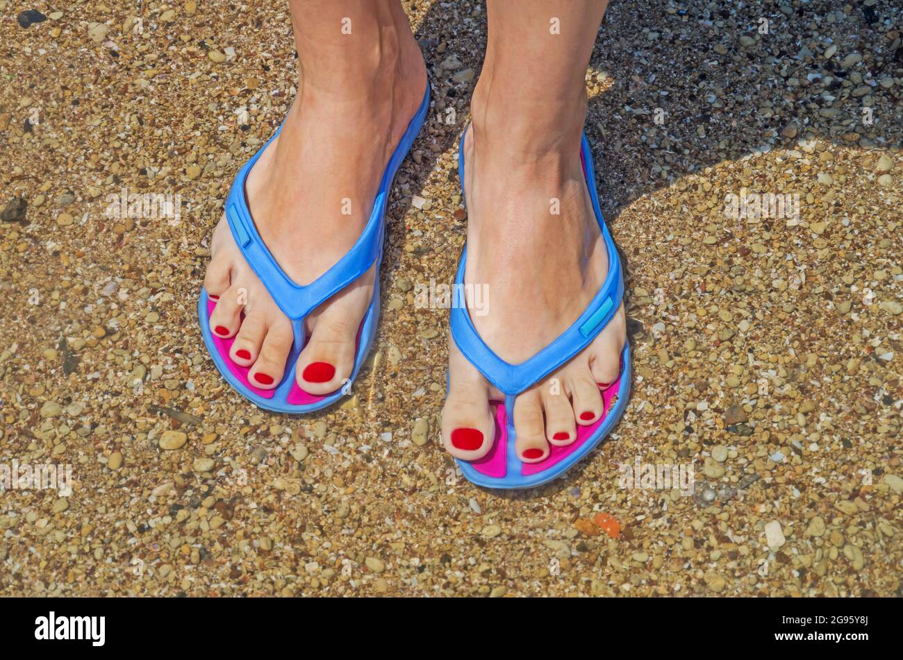 Pies de mujer con clavos pintados en chanclas en la playa al borde del agua  Fotografía de stock - Alamy
