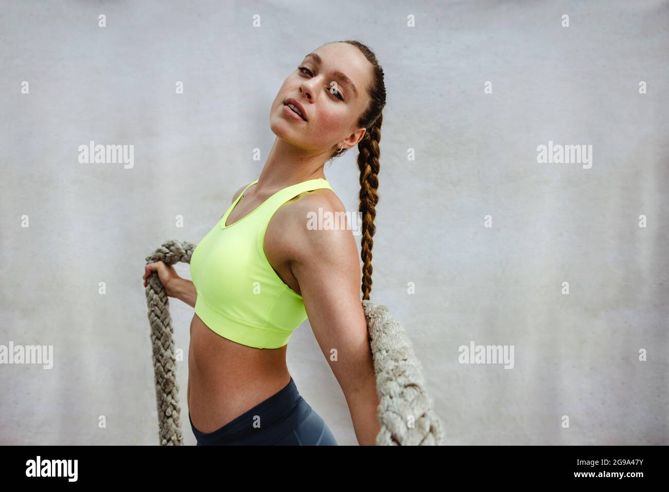 Ajusta a la mujer en ropa deportiva con cuerda de batalla mirando la cámara. Mujer atleta segura relajándose después de hacer ejercicio. Foto de stock