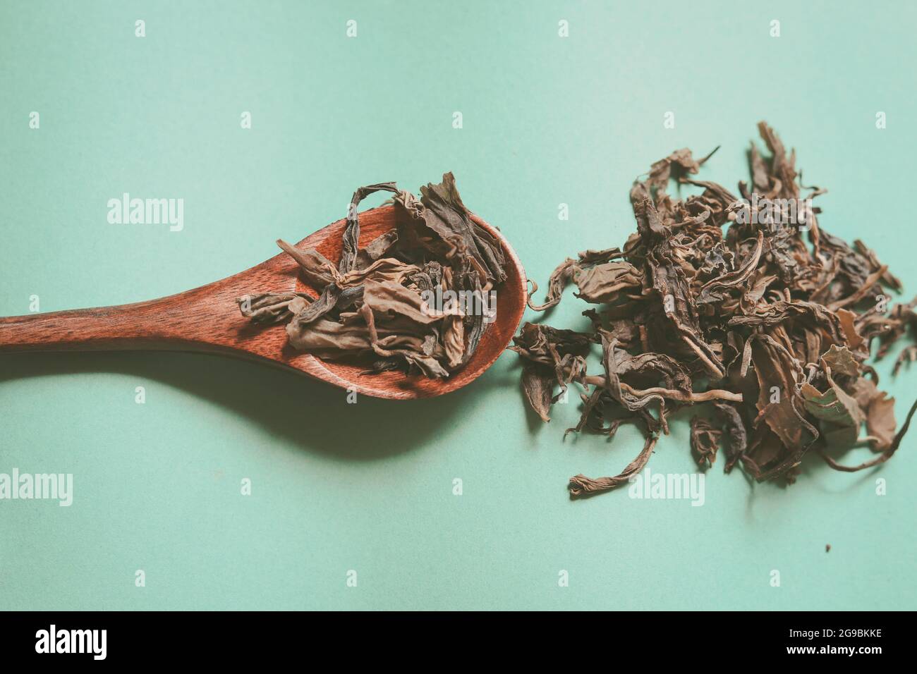 Una cuchara de madera con hojas secas de cannabis sativa o marihuana sobre un fondo verde con un espacio de copia Foto de stock