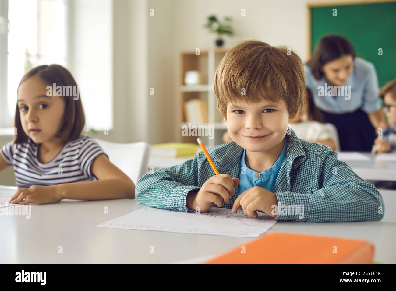 Retrato de un lindo estudiante de la escuela primaria sentado en su escritorio en el salón de clases Foto de stock