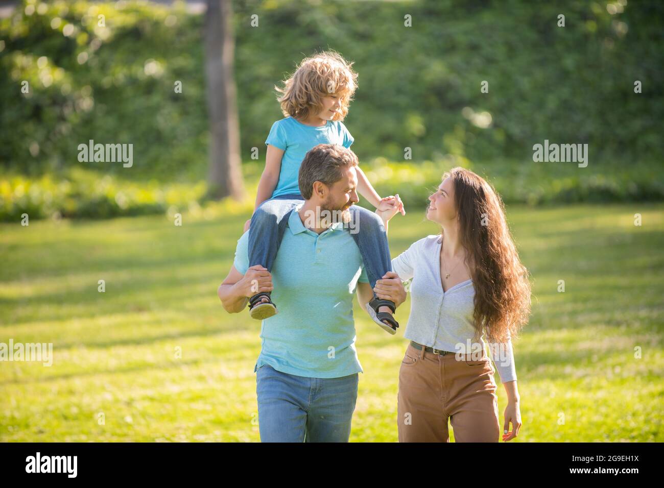 Feliz familia de madre y padre llevando niño niño en los hombros verano al aire libre, de crianza Foto de stock
