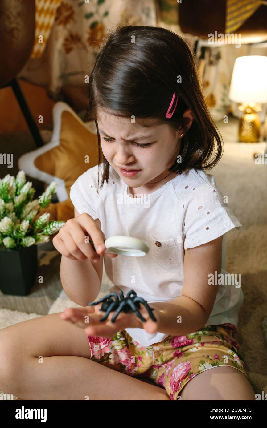 Chica disgustada jugando observando insectos de juguete con una lupa Foto de stock