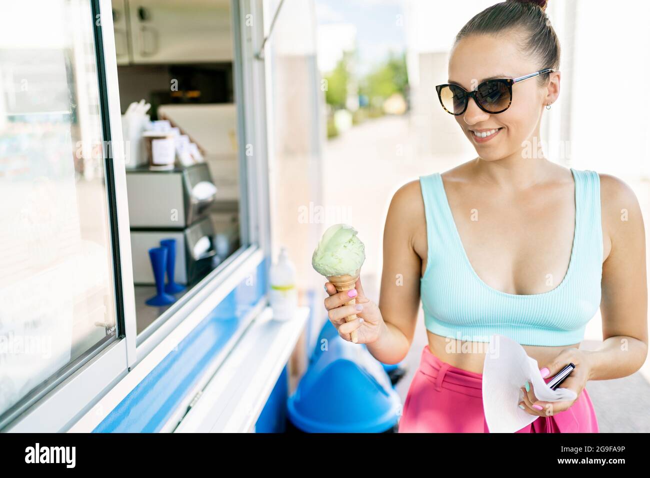 Cliente feliz comprando helado de salón, camión, furgoneta o kiosco. Comida para llevar gelato en verano. Mujer sonriente sosteniendo un cono de helado en la mano. Foto de stock
