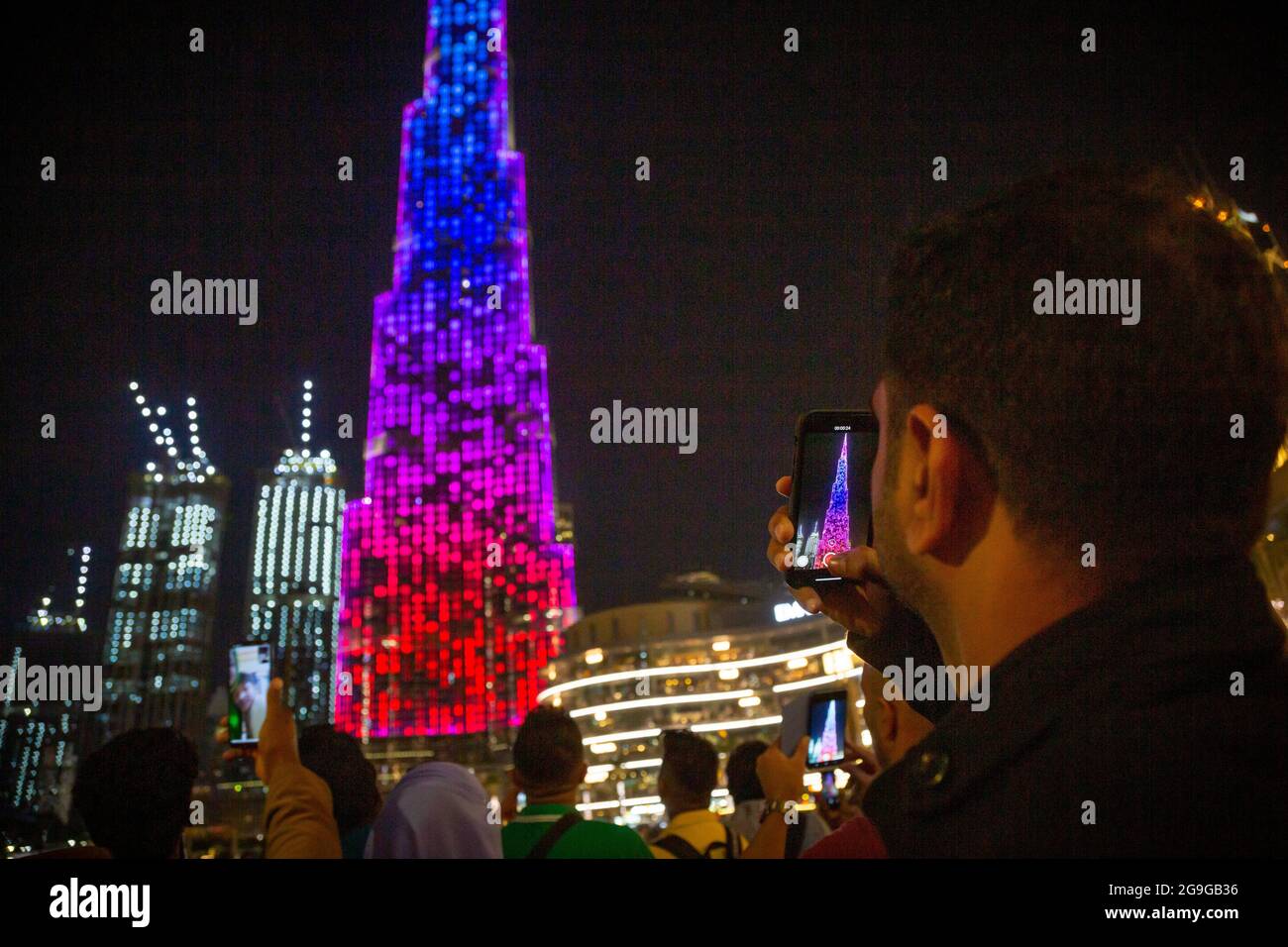 Un hombre graba el espectáculo de luces en Burj Khalife, Dubai, EAU. --- Burj Khalifa, el edificio más alto del mundo, es el telón de fondo para una iluminación espectacular Foto de stock