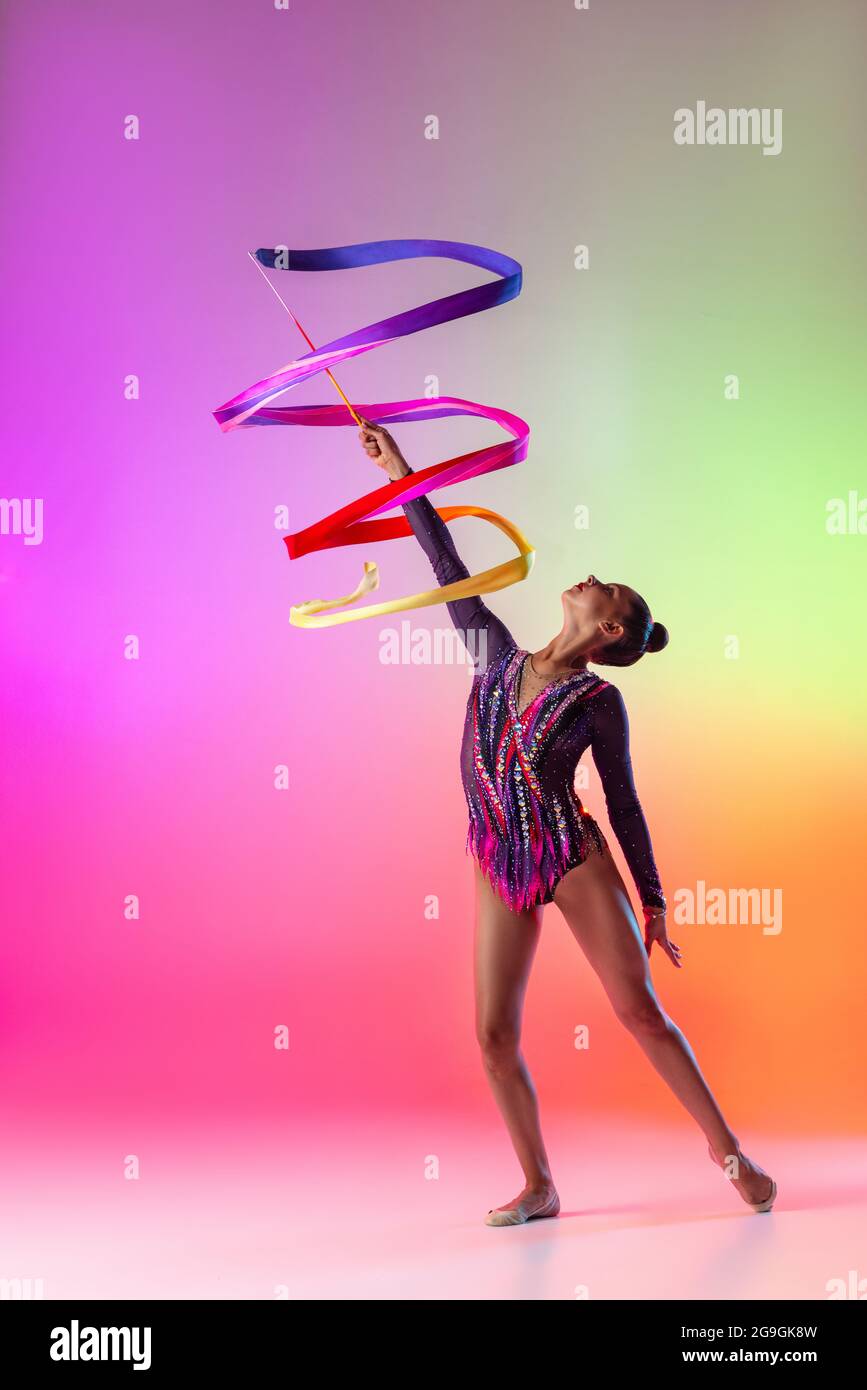 Joven profesional femenino ejercicio de gimnasia rítmica con cinta  brillante aislada sobre fondo de neón multicolor Fotografía de stock - Alamy