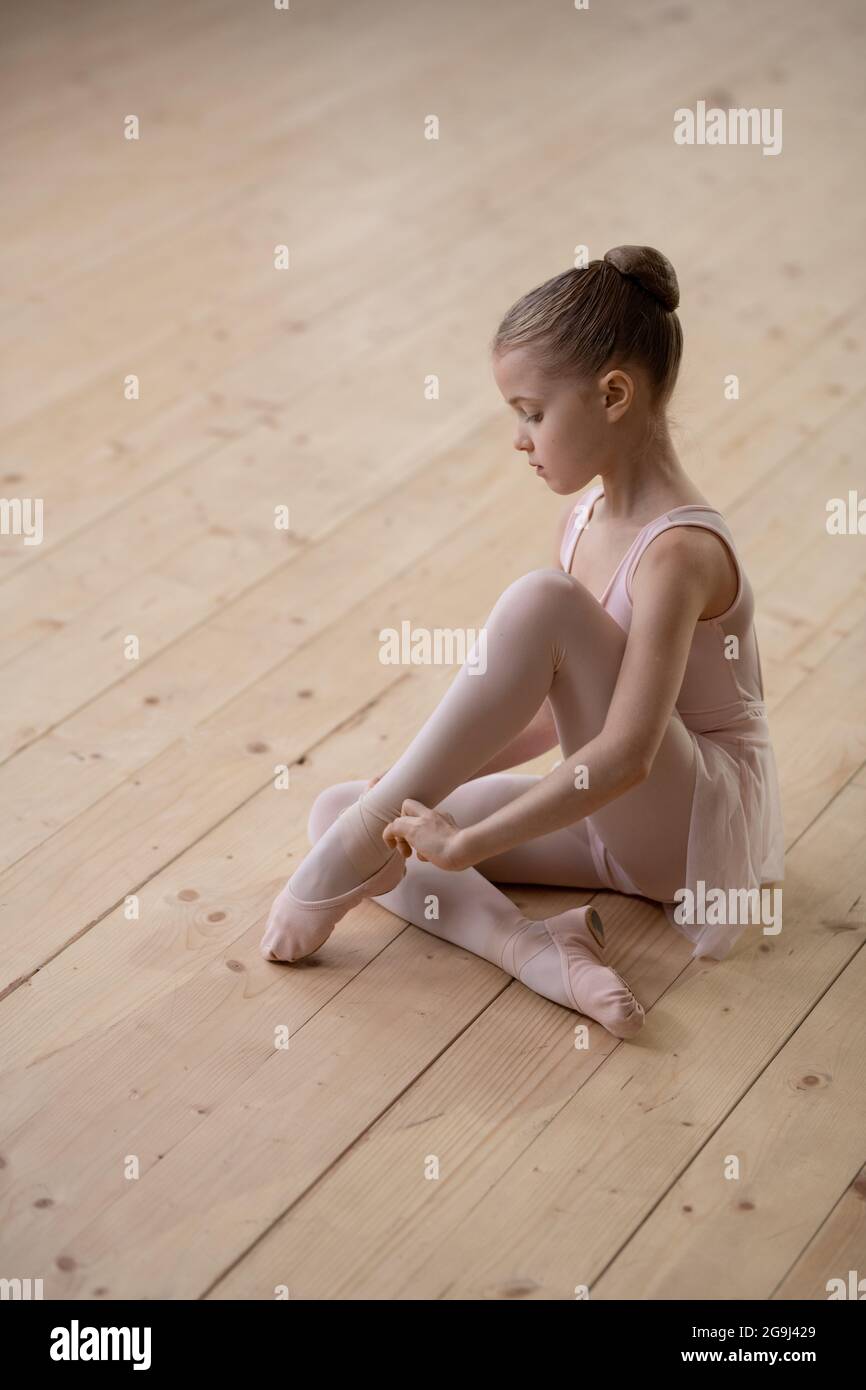 Retrato de una niña de bailarina mirando la cámara mientras estaba sentada en el piso de madera en el club de baile Foto de stock
