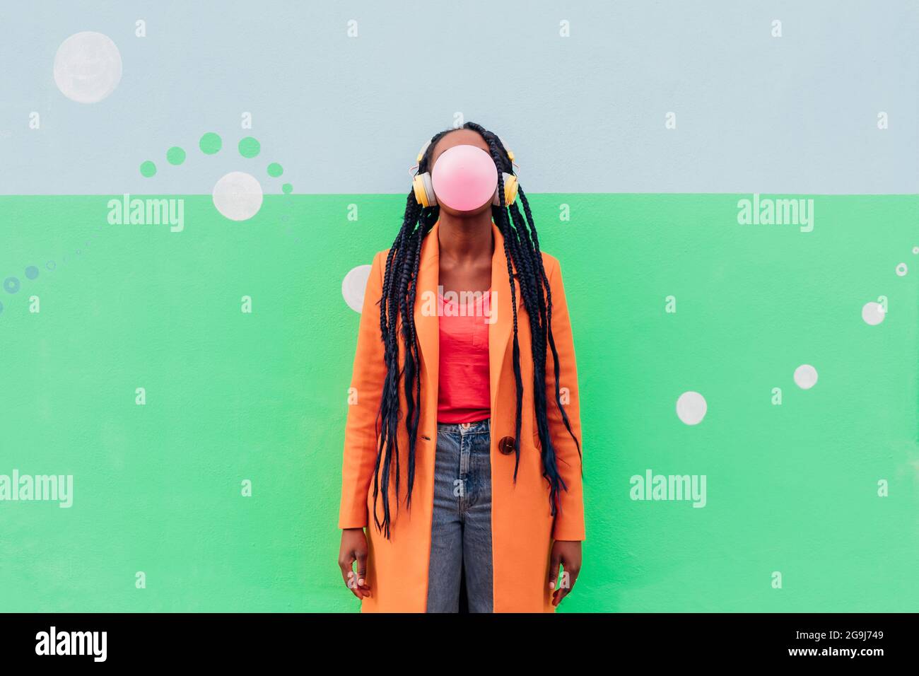 Italia, Milán, mujer con estilo con auriculares que soplan goma contra la pared Foto de stock