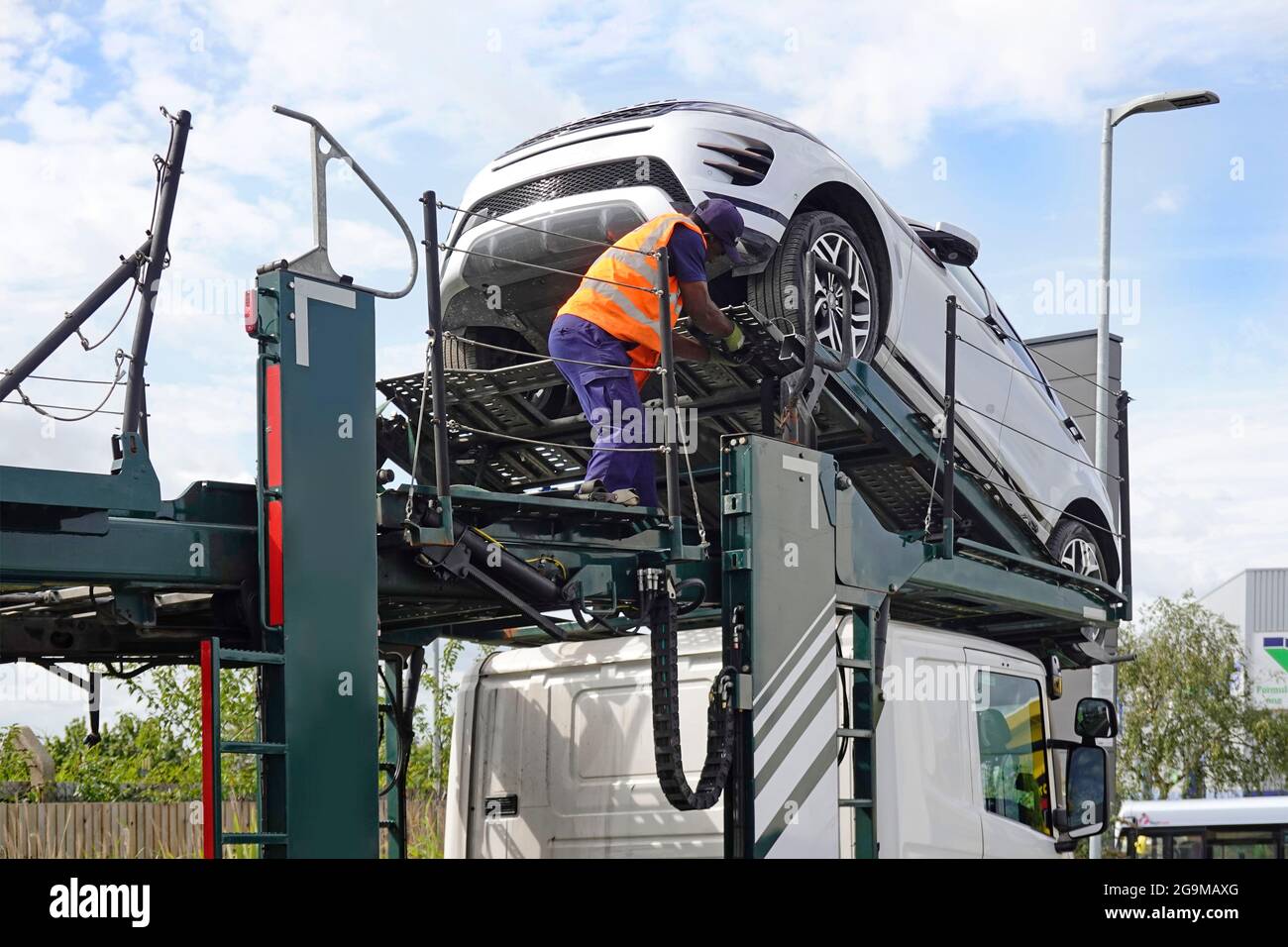 Conductor de transporte de coches que trabaja con chaqueta de alta visibilidad en el último vehículo que se conduce por la rampa superior sobre la entrega de la cabina de camión al concesionario Inglaterra Reino Unido Foto de stock