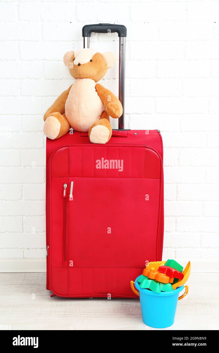 Maleta roja con oso de peluche y juguetes para niños sobre fondo blanco de  pared de ladrillo Fotografía de stock - Alamy