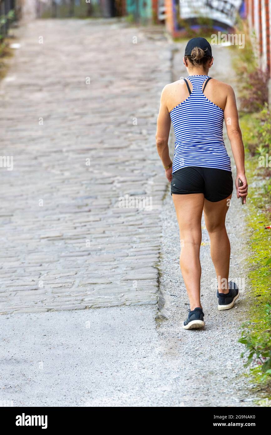 mujer joven haciendo ejercicio con pantalones cortos y chaleco con gorra de  béisbol bajo el sol del verano caminando por una calle empedrada para  mantenerse en forma Fotografía de stock - Alamy
