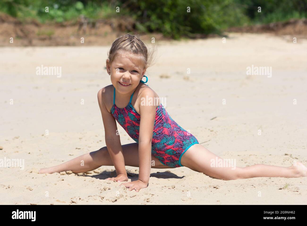 Caucásica niña de cinco años en traje de baño en la playa de arena haciendo piernadividida