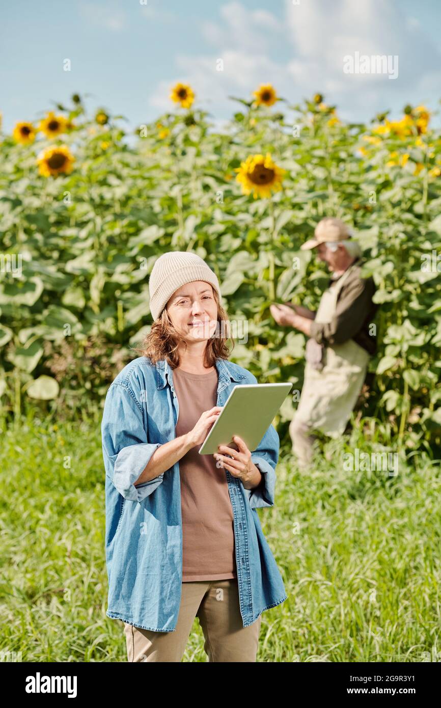 Mujer campesina madura en ropa de trabajo de pie frente a la cámara y  usando touchpad contra campo de girasol y hombre maduro encendido día  soleado Fotografía de stock - Alamy
