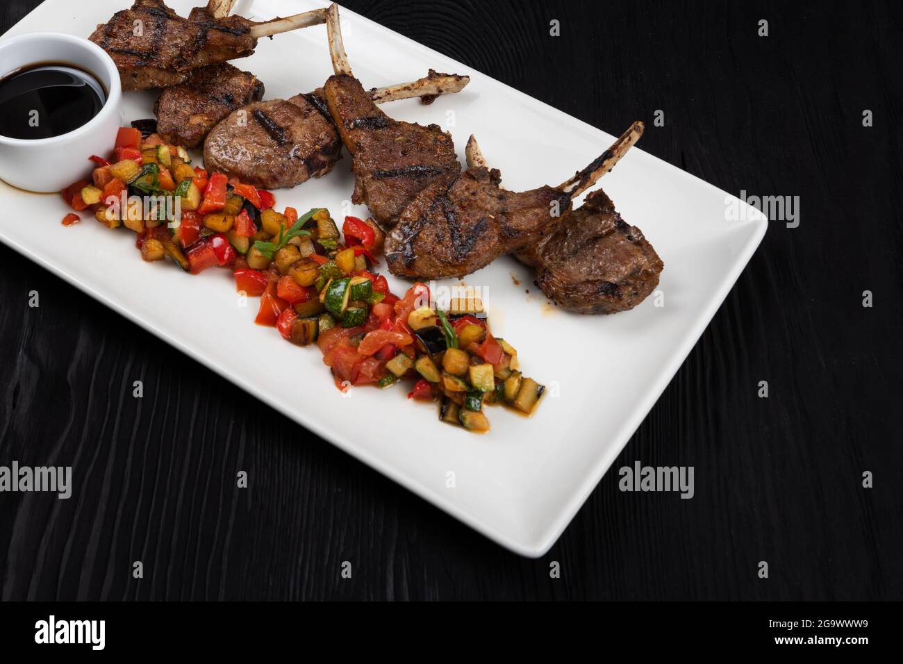 Costillas de cordero asadas con verduras sobre plato blanco sobre fondo  negro de madera Fotografía de stock - Alamy